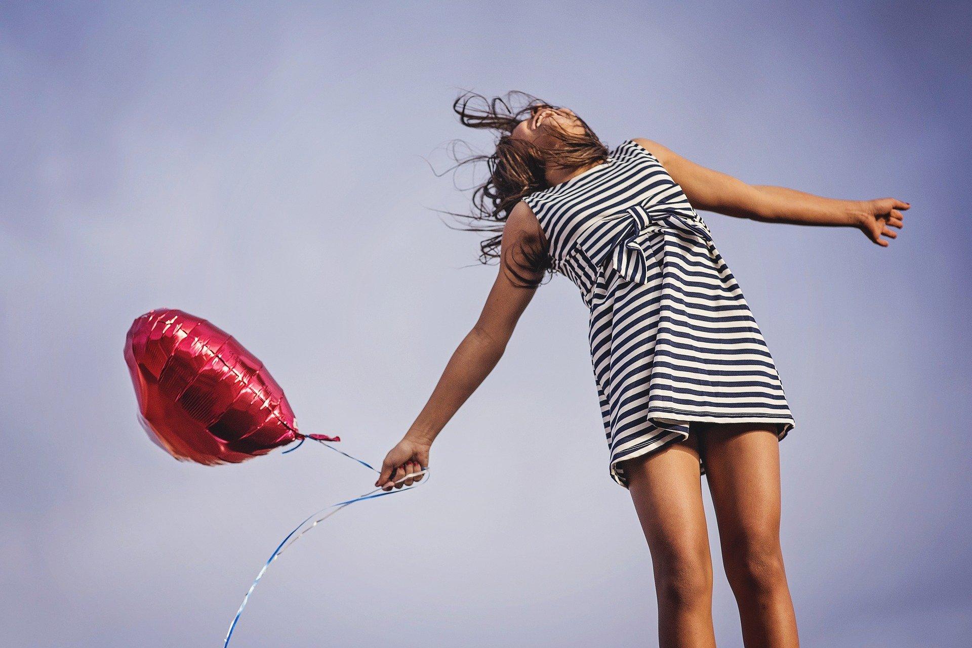 Imagem mostra mulher feliz com balão vermelho nas mãos - frases de felicidade