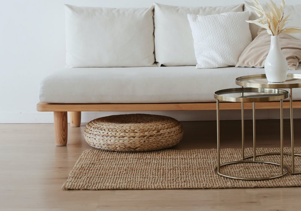 Sala com sofá branco, tapete marrom e piso laminado em madeira claro