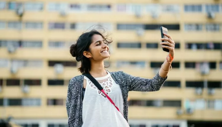 Mulher em frente a um prédio tirando uma foto de si mesma com celular