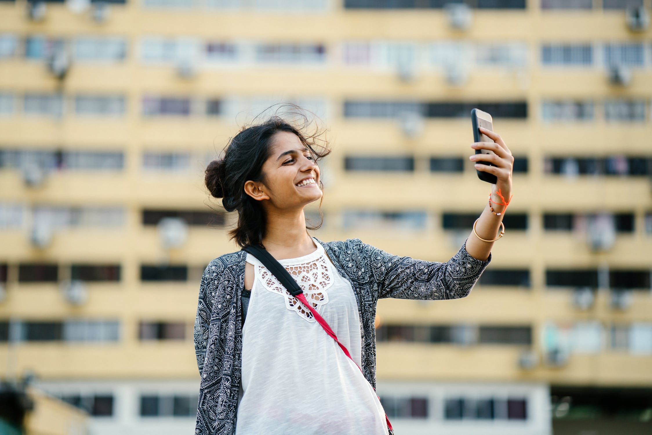 Mulher em frente a um prédio tirando uma foto de si mesma com celular