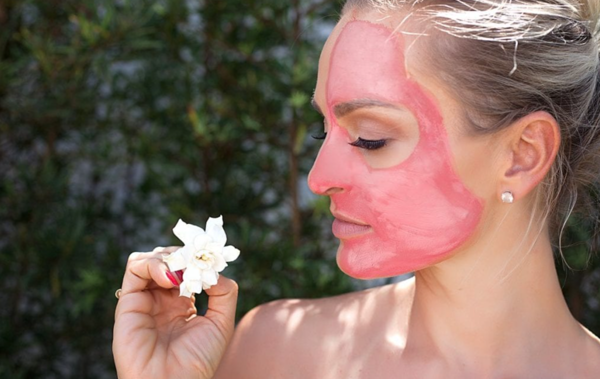 mulher com máscara facial de argila rosa segundo uma flor