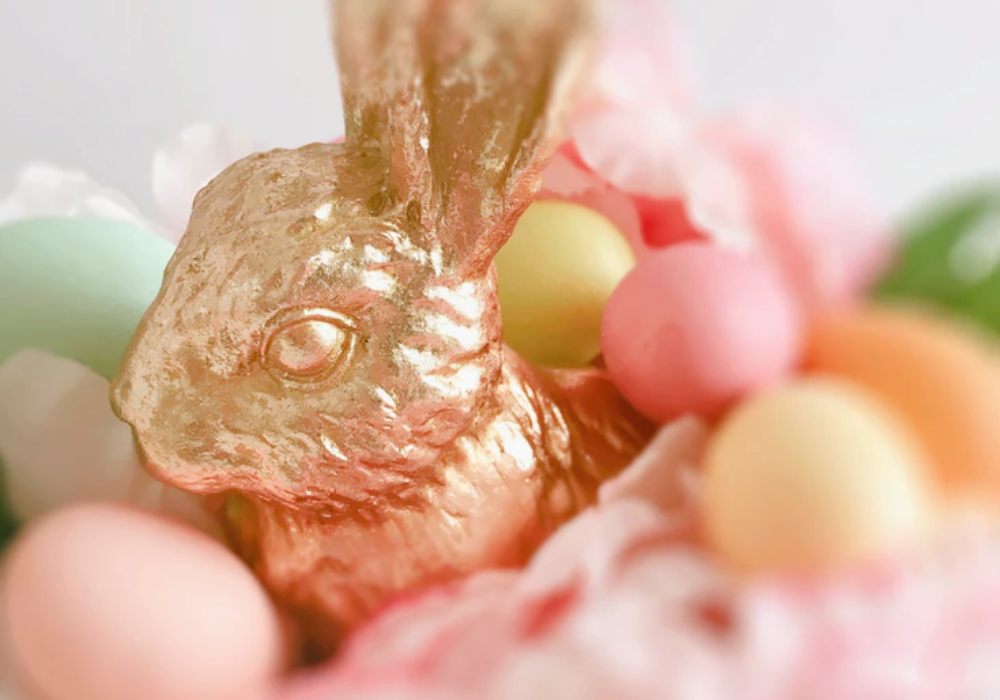 coelho de chocolate embalado em papel dourado com ovos de chocolate ao redor