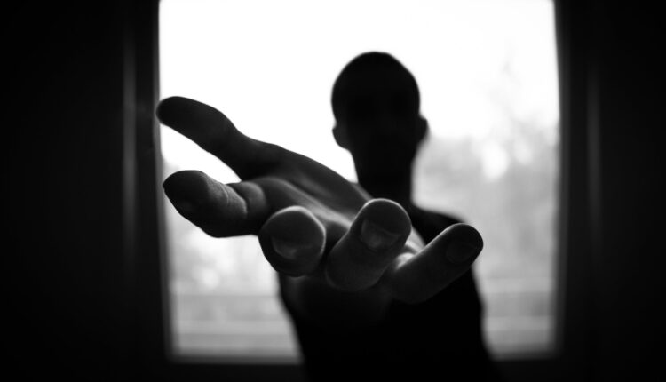 imagem em preto e branco com contraste mostra homem esticando a mão