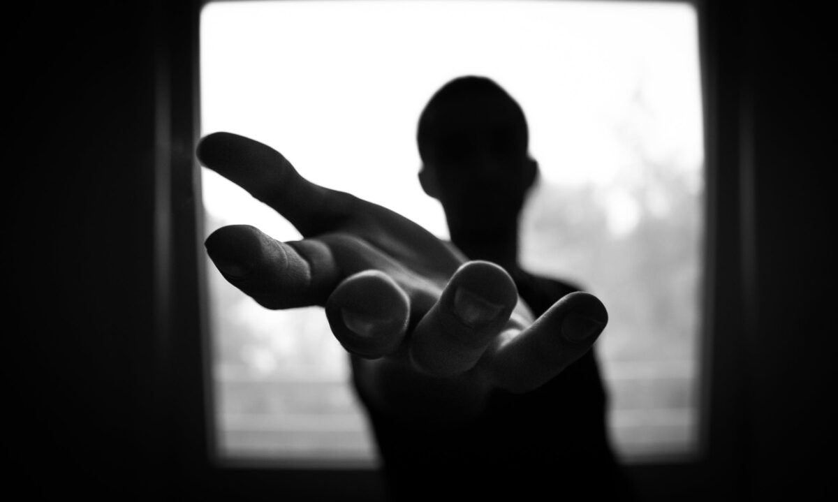 imagem em preto e branco com contraste mostra homem esticando a mão