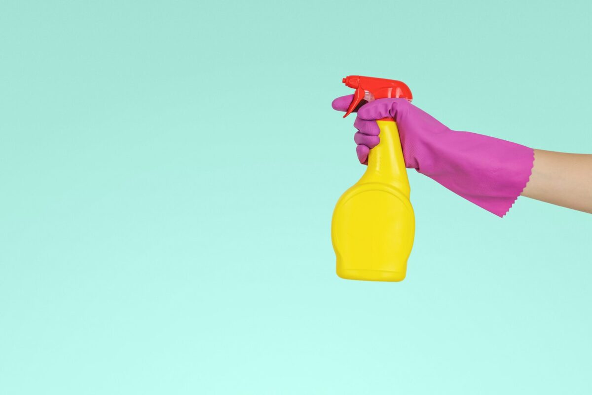 imagem mostra mão com luvas segurando spray de limpeza