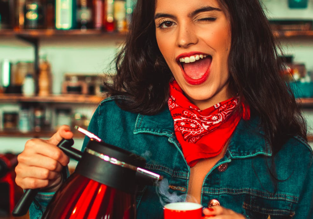 imagem mostra mulher piscando e servindo uma xícara de café
