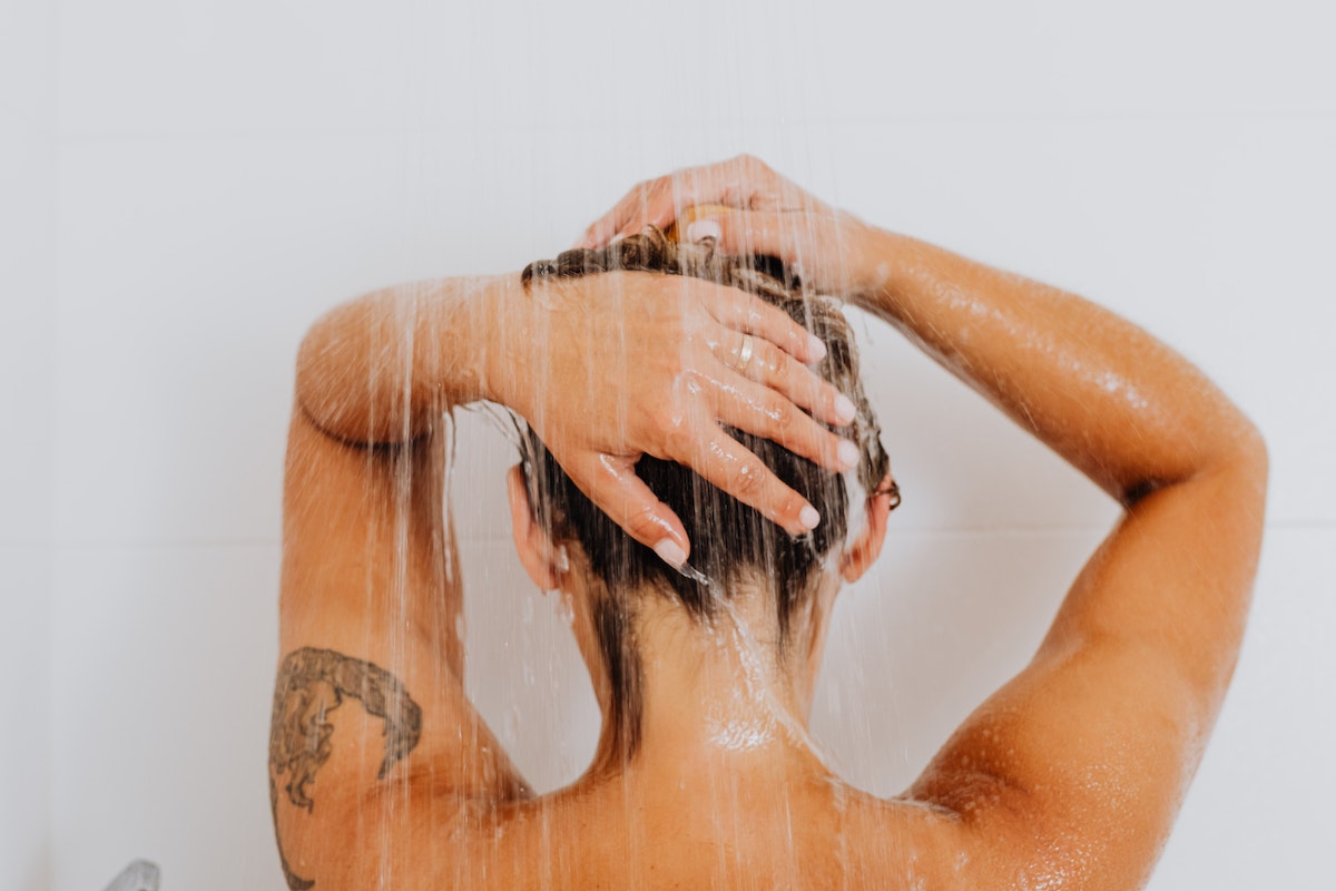 Mulher com tatuagem no braço, lavando os cabelos no banho