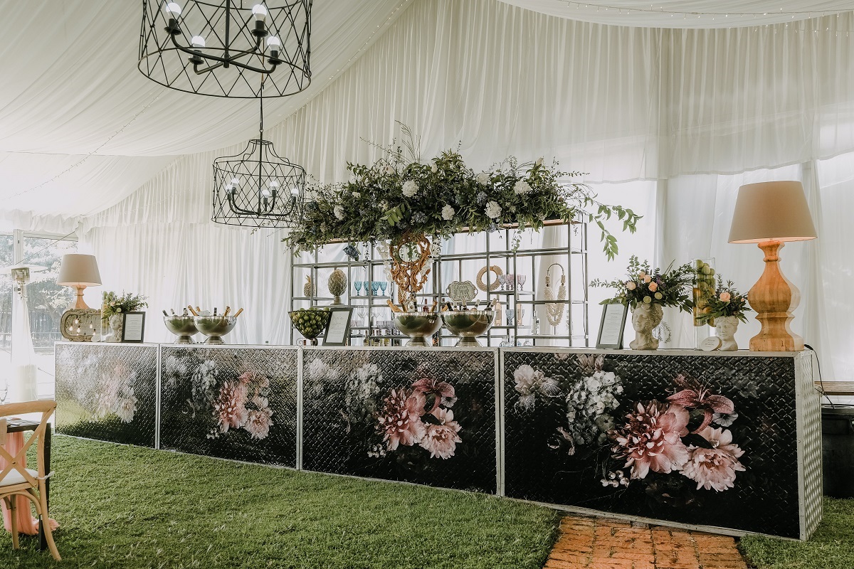 pequeno balcão todo decorado com flores e, atrás dele, há uma estante com mais plantas dispostas pelas prateleiras