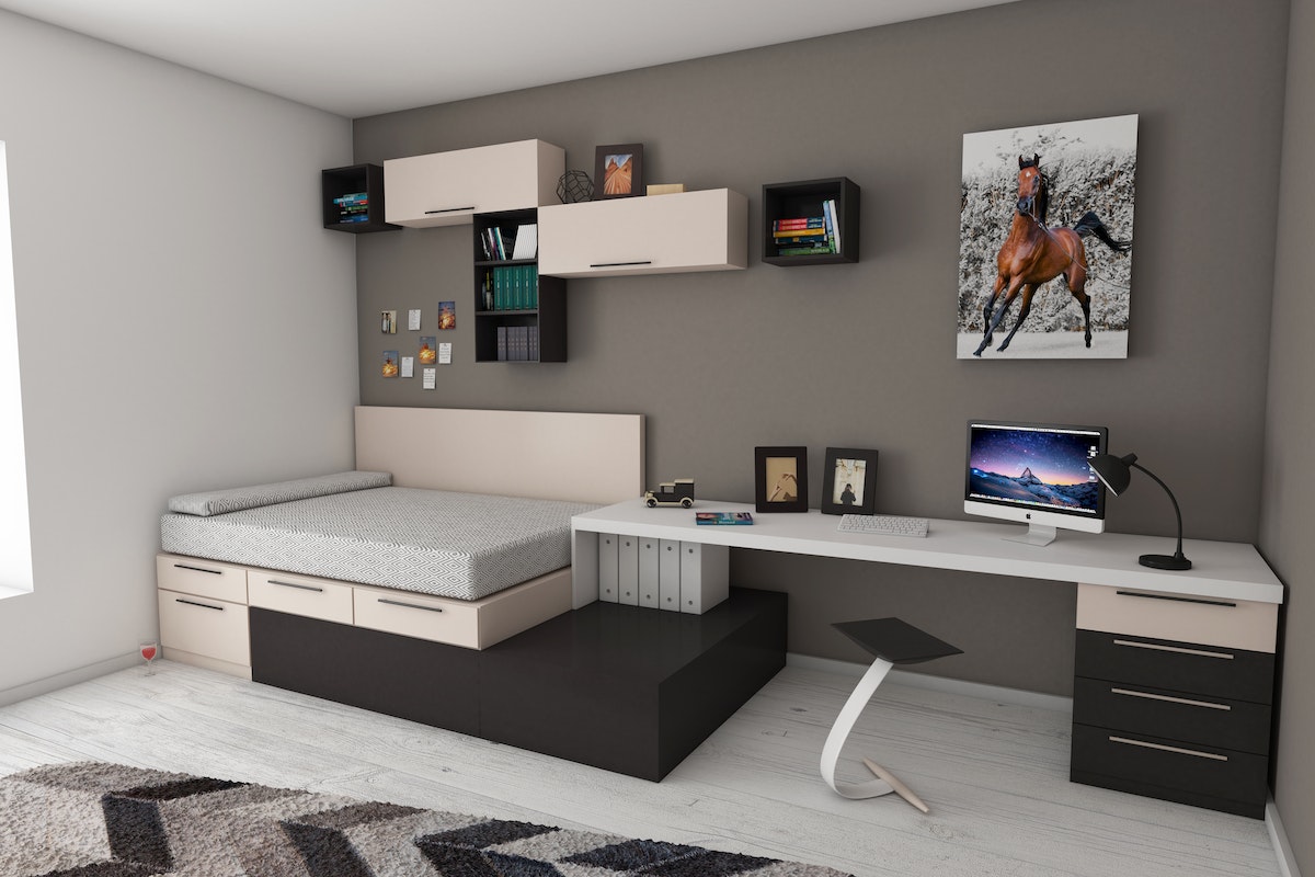 Quarto cinza, branco e marrom, com decoração futurista, onde a cama é integrada aos armários e a mesa de trabalho. Em cima da cama há várias prateleiras com livros e, em cima da mesa, um quadro de um cavalo