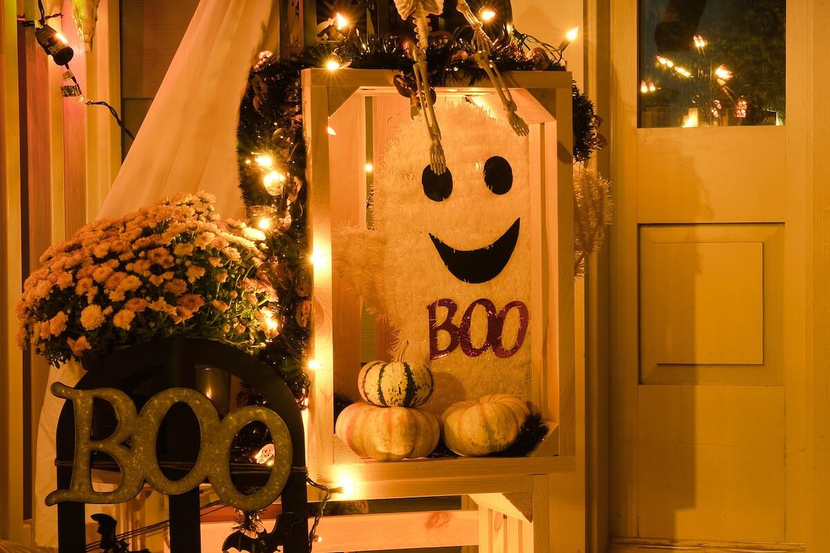 espaço no canto da porta decoração para o halloween com abóboras de verdade, desenhos de fantasmas, letreiro BOO e várias luzes espalhadas