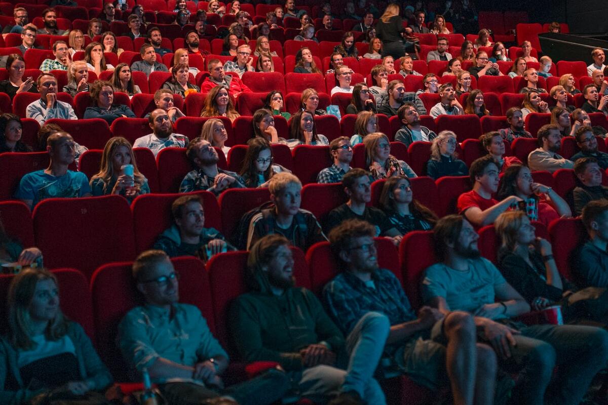 foto de diversas pessoas diferentes sentadas em poltronas vermelhas em uma sala de cinema