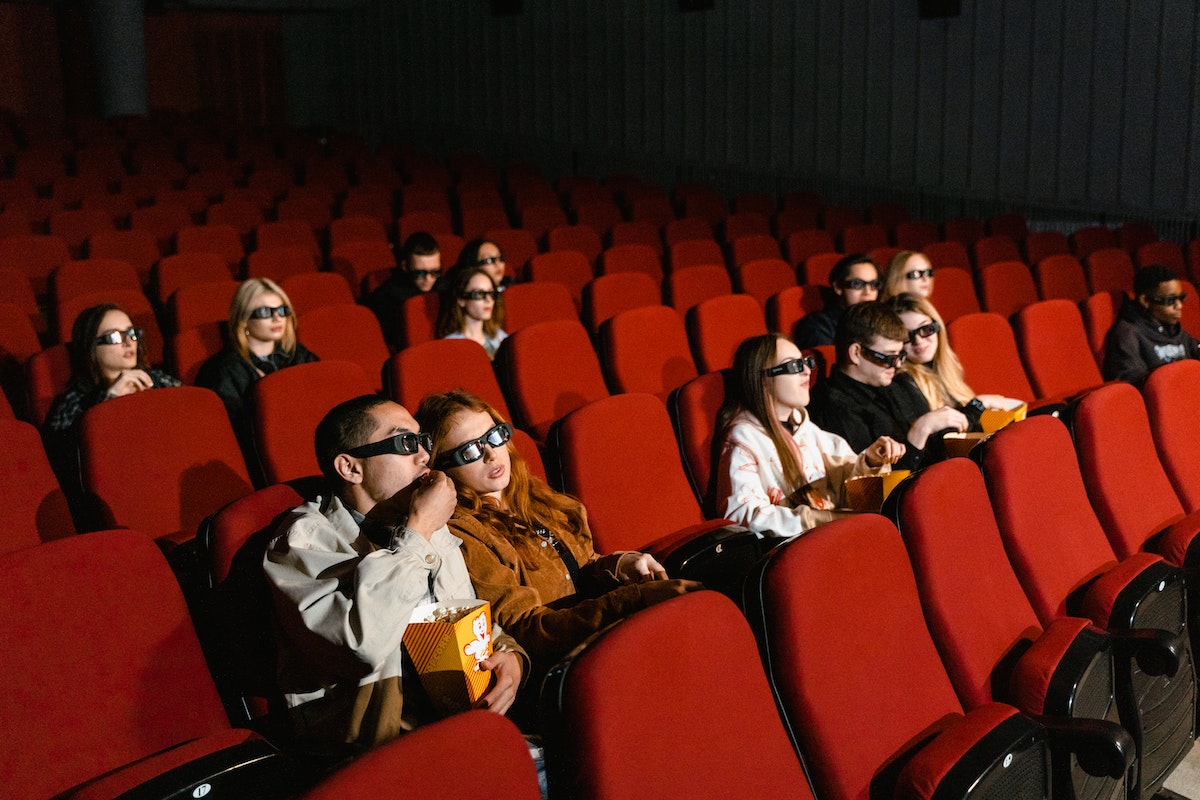Várias pessoas sentadas no cinema sentadas, usando óculos 3D e comendo pipoca