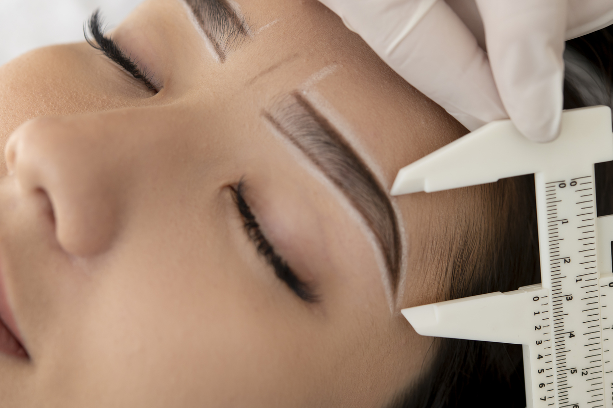 Imagem de uma mulher deitada com um profissional de micropigmentação medindo a sua sobrancelha