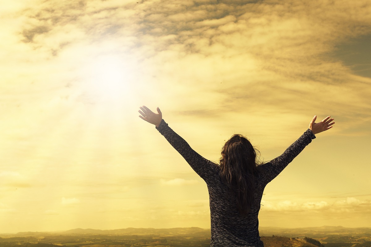 Imagem de uma pessoa com os braços abertos olhando para o céu e rezando