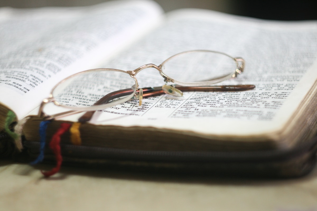 Imagem de uma bíblia sabrada aberta com um óculos sobre ela em cima de uma mesa