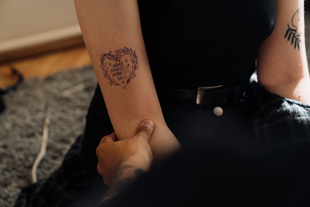 Imagem de um tatuador segurando um braço feminino e fazendo uma tatuagem