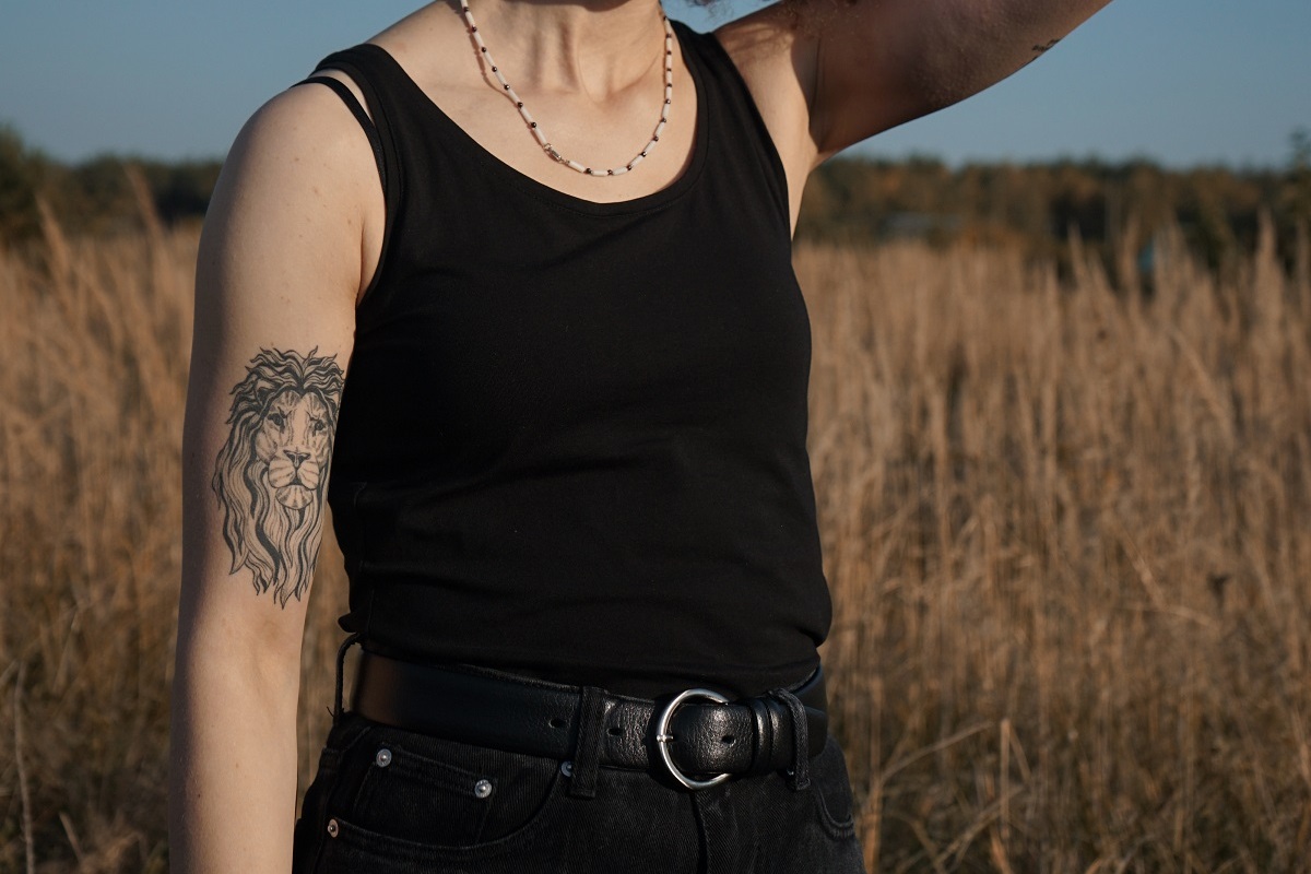 Imagem de um tronco feminino, com um campo no fundo, esta mulher tem uma tatuagem no braço direito