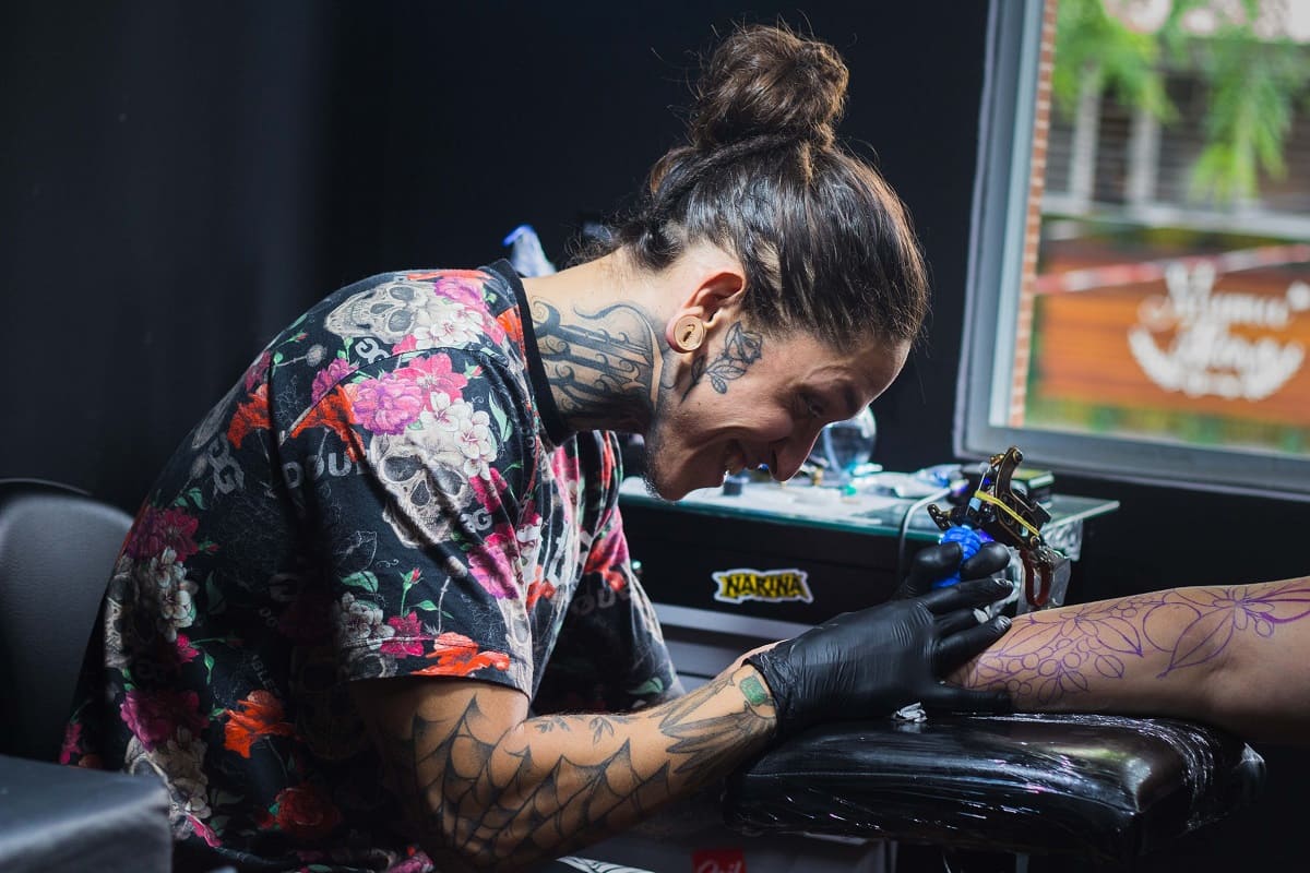Imagem de um tatuador sorrindo e fazendo o seu trabalho em um braço