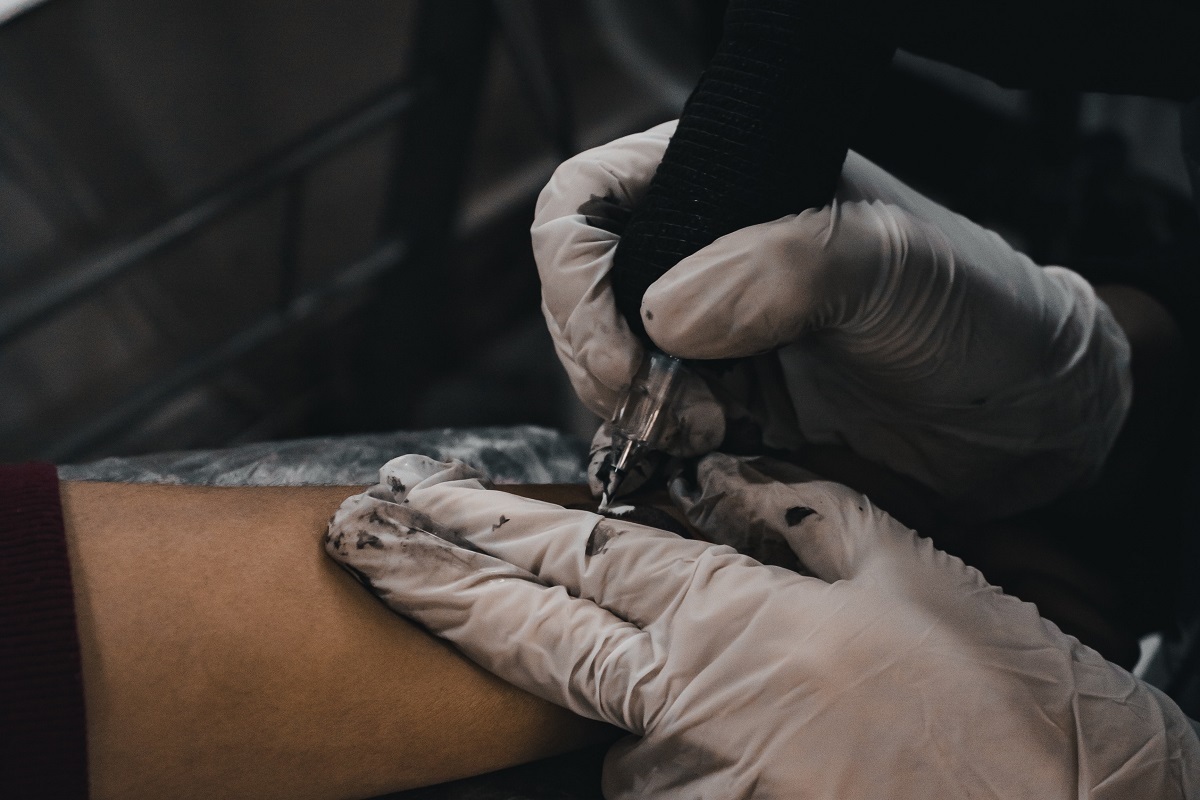 Imagem de um taduador fazendo uma tatuagem em um braço feminino