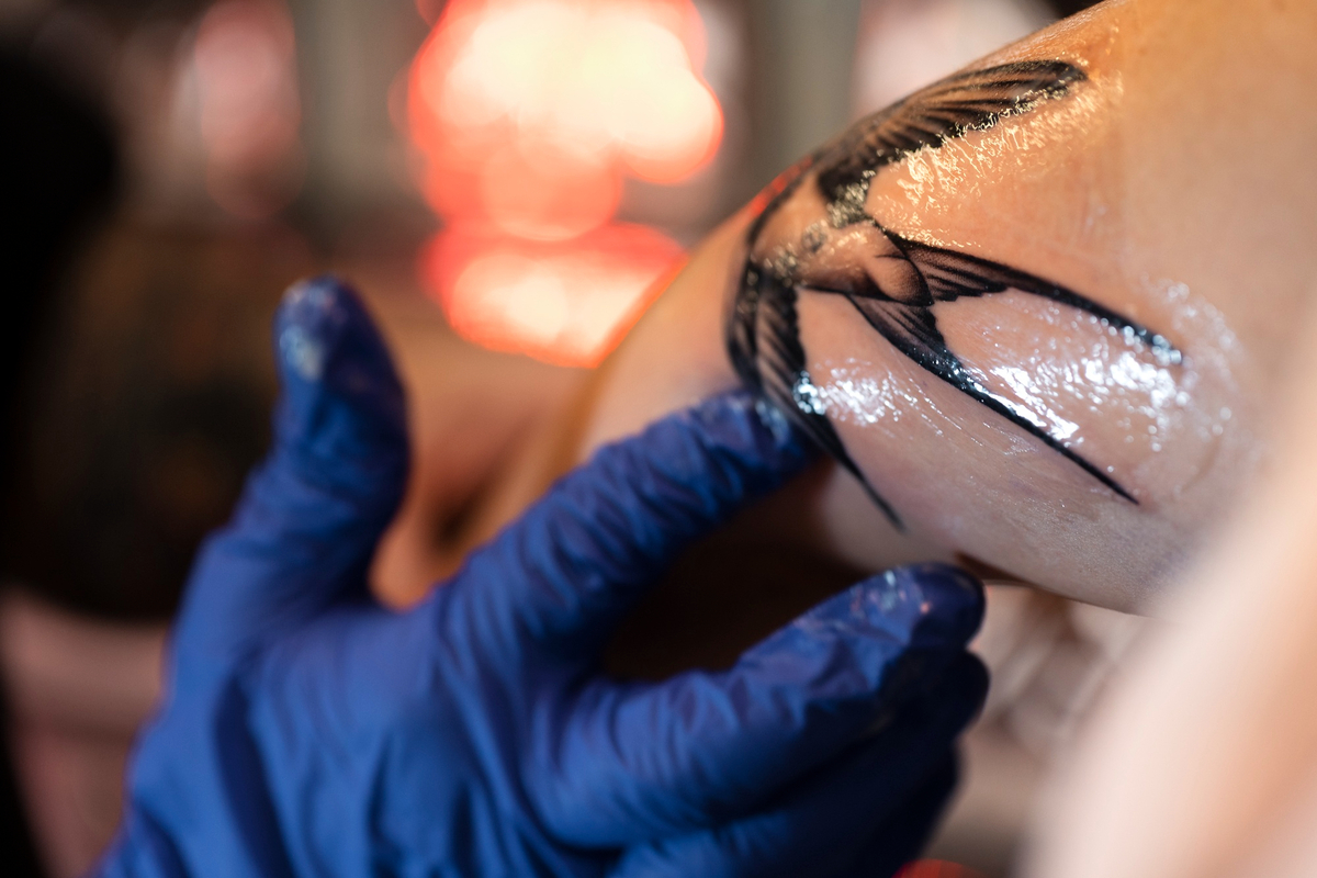 Um tatuador enrolando plástico filme em uma tatuagem feita no braço do cliente