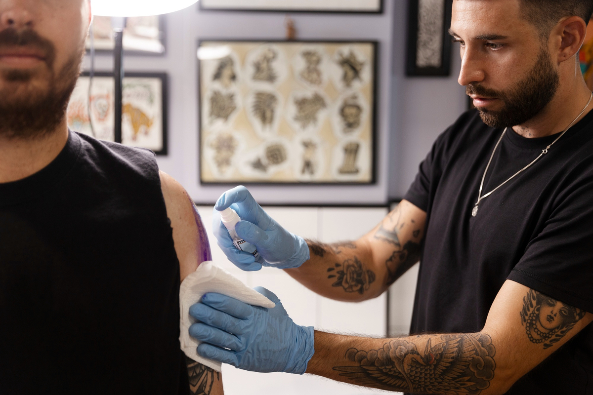 Imagem de um tatuador higienizando o bralço de um cliente, onde vai tatuar
