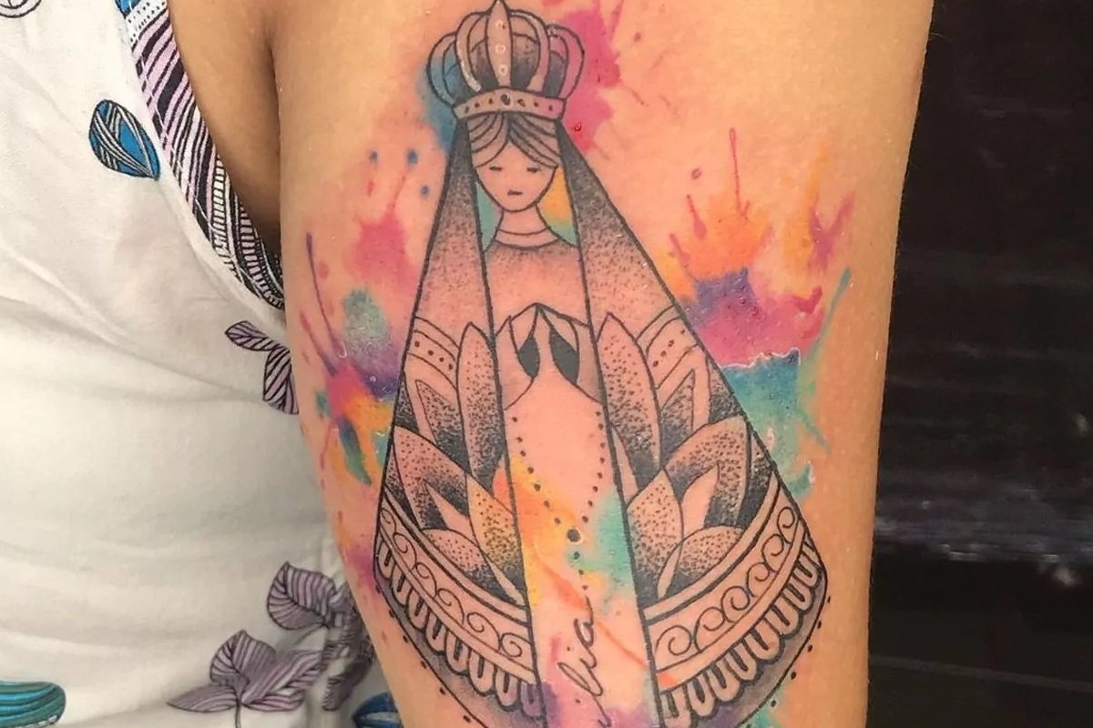 Imagem de um braço feminino com uma tatuagem de Nossa Senhora Aparecida em aquarela