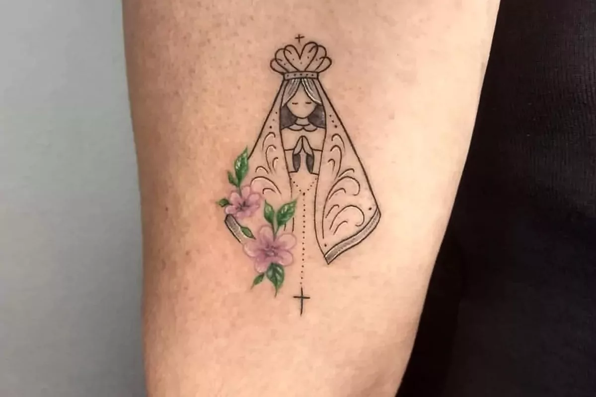 Imagem de um antebraço com uma tatuagem de Nossa Senhora Aparecida com flores rosas