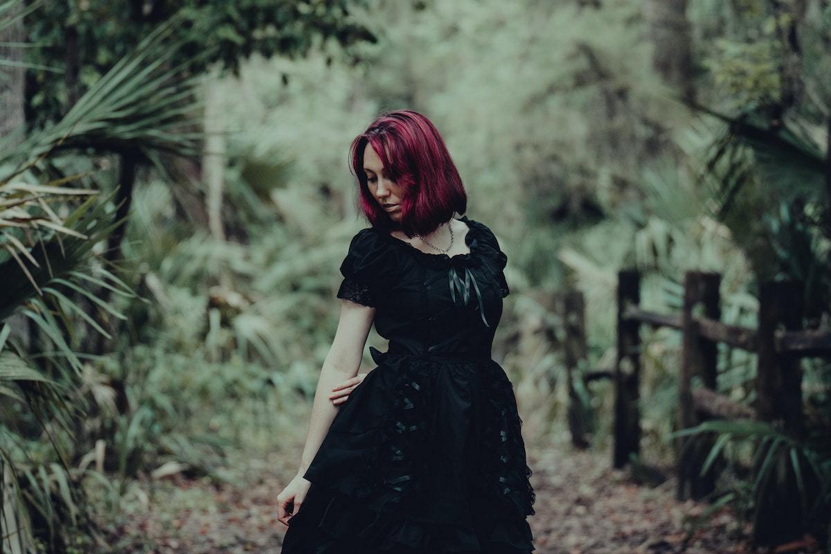 Mulher em trilha de bosque com cabelo marsala e roupa preta