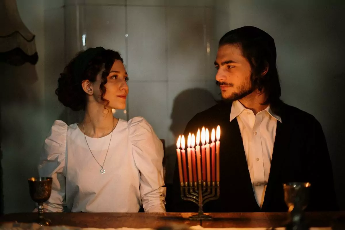 Casal judeu se olhando enquanto estão sentados lado a lado em lugar iluminado por velas