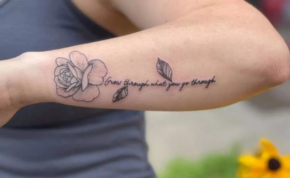 mulher com braço com tatuagem de frase sendo o caule de uma flor
