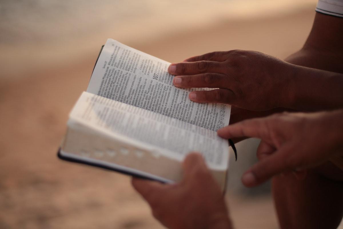 Dois homens aparentemente sentados com bíblia aberta apontando para algo no livro sagrado enquanto parecem conversam entre si