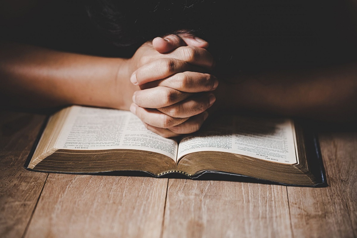 Oração e jejum: A imagem mostra uma pessoa com as mãos cruzadas indicando como oração em cima de uma Bíblia