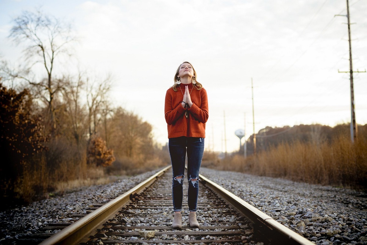 Oração e jejum: A imagem mostra uma pessoa orando e ela está sobre trilhos de trem 