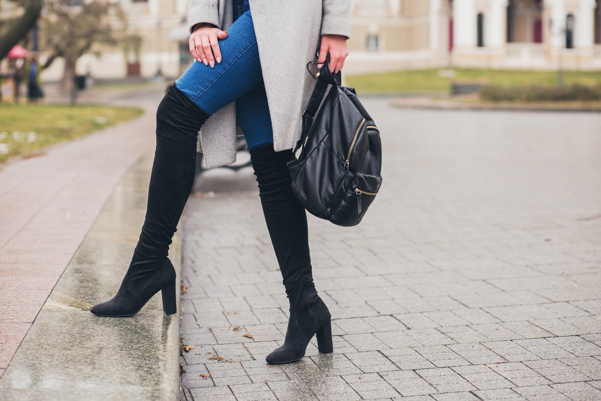 Sapatos femininos: A imagem mostra uma mulher usando uma bota de cano longo e uma bolsa, ambas nas cores pretas. 