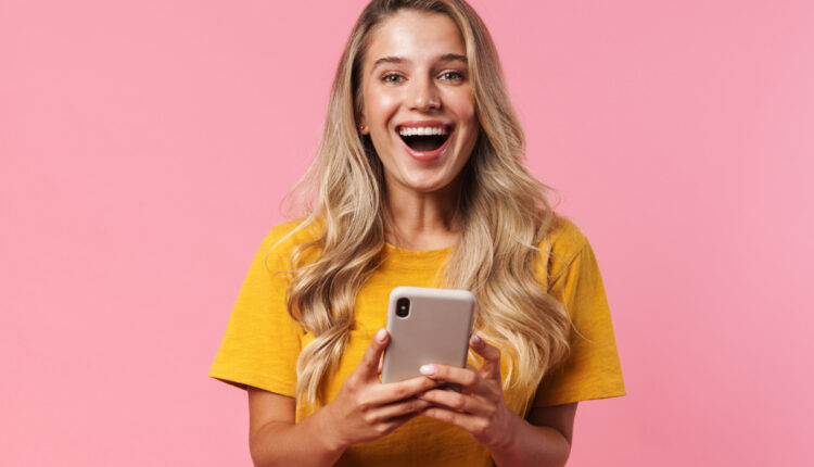 Mulher loira sorrindo segurando celular; conheça 80 opções de legenda para foto nas redes sociais