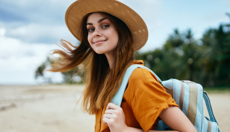 Mulher sorrindo para a câmera, usando chapéu e mochila; veja 50 frases para viajantes