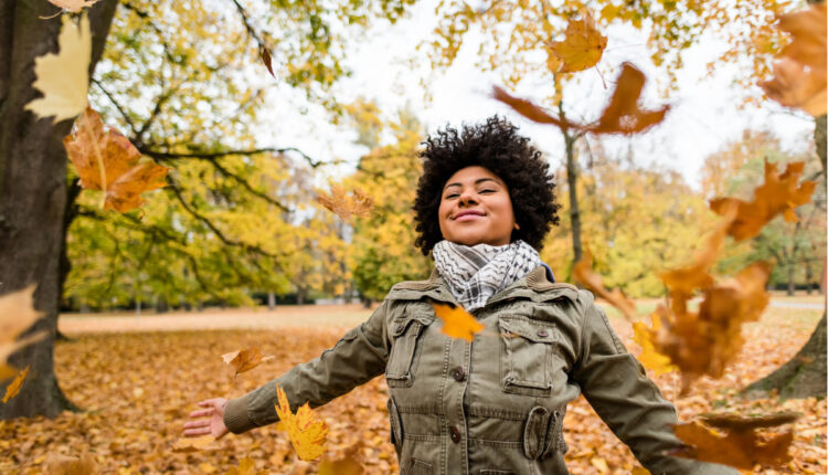 Escolha sua legenda para foto no outono; na foto, mulher feliz em meio às árvores e folhas outonais